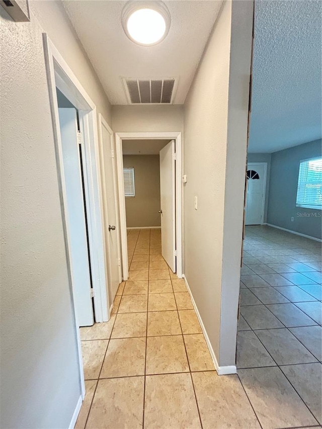 corridor with a textured ceiling and light tile patterned floors