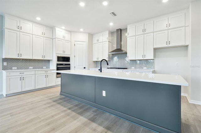 kitchen featuring oven, white cabinets, wall chimney exhaust hood, and an island with sink