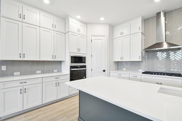 kitchen with built in microwave, wall chimney range hood, gas stovetop, oven, and white cabinets