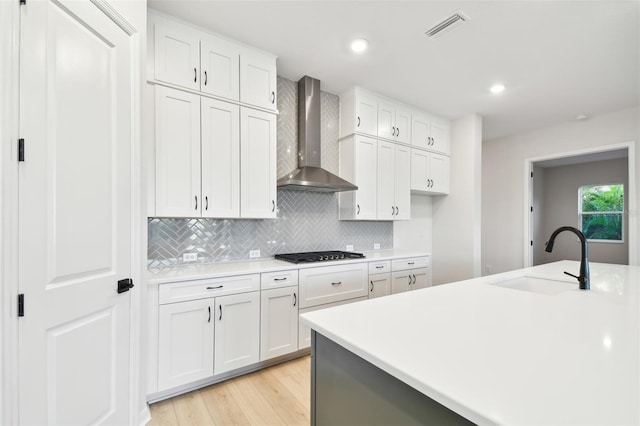 kitchen featuring backsplash, sink, wall chimney range hood, white cabinets, and stainless steel gas stovetop