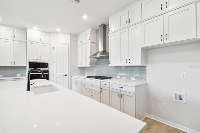 kitchen with wall chimney exhaust hood, stainless steel appliances, sink, light hardwood / wood-style flooring, and white cabinets