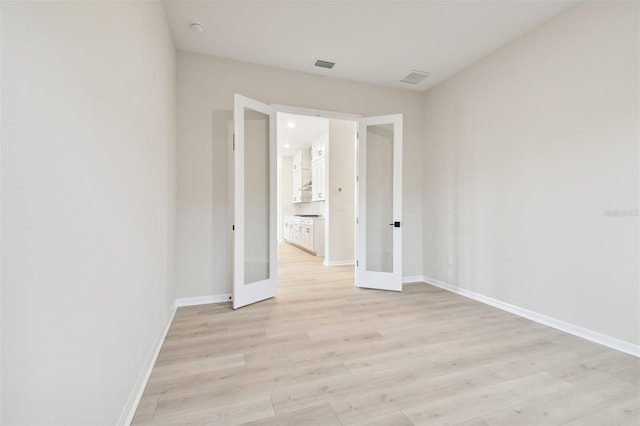 spare room with french doors and light hardwood / wood-style flooring