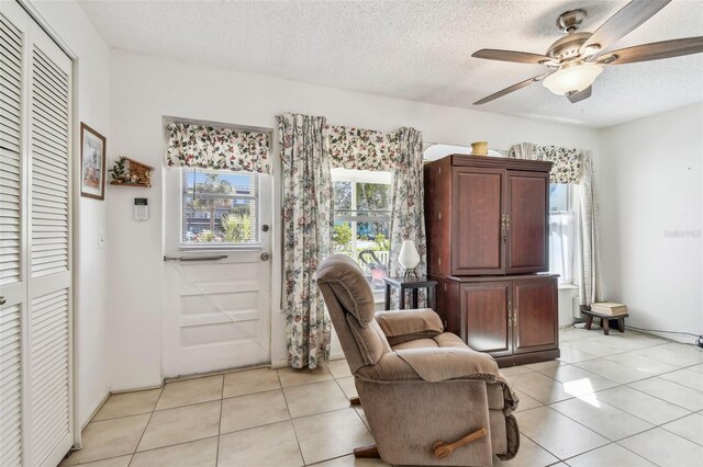 living area featuring ceiling fan, light tile patterned floors, and a textured ceiling