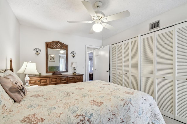 bedroom with a textured ceiling, ceiling fan, and multiple closets