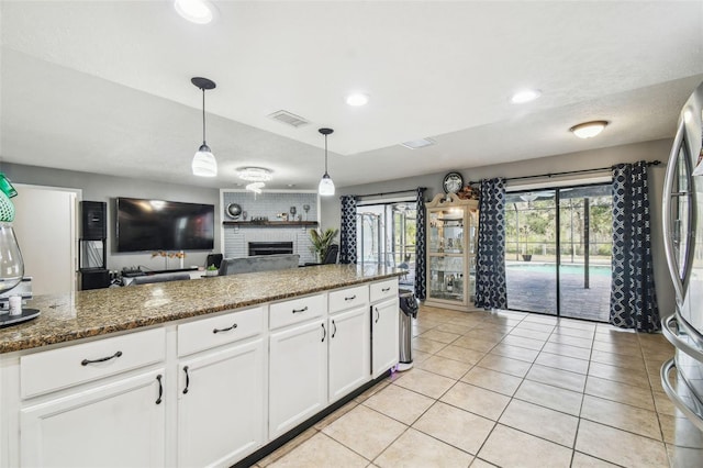 kitchen featuring decorative light fixtures, white cabinetry, dark stone counters, a fireplace, and stainless steel fridge