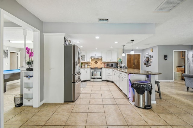 kitchen featuring decorative light fixtures, white cabinetry, a breakfast bar area, stainless steel appliances, and light tile patterned floors