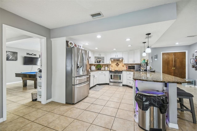 kitchen featuring dark stone countertops, kitchen peninsula, hanging light fixtures, stainless steel appliances, and white cabinets