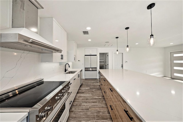 kitchen featuring high end range, white refrigerator, wall chimney range hood, sink, and white cabinetry