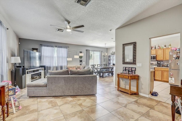 tiled living room with a textured ceiling and ceiling fan with notable chandelier