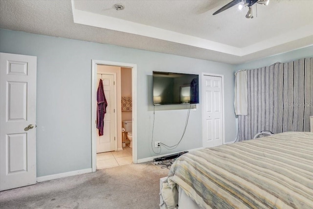 carpeted bedroom featuring a textured ceiling, ceiling fan, ensuite bathroom, and a tray ceiling