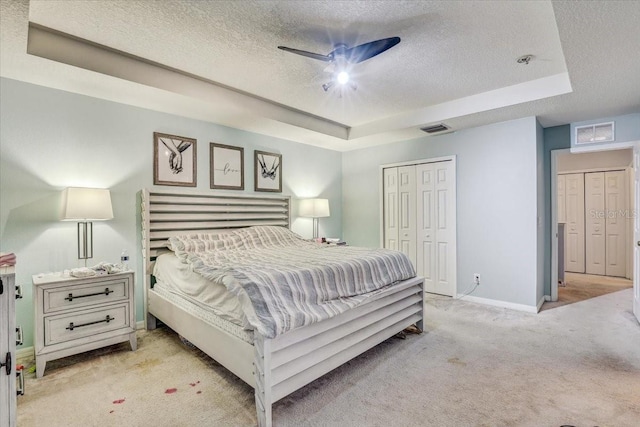 bedroom featuring a textured ceiling, a tray ceiling, light colored carpet, ceiling fan, and a closet