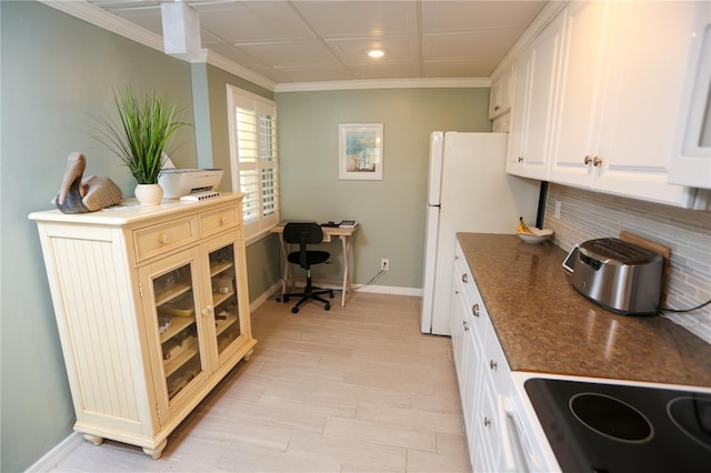 kitchen featuring white cabinets, white refrigerator, crown molding, dark stone countertops, and cooktop