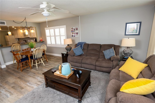 living room with ceiling fan with notable chandelier, wood-type flooring, and a textured ceiling