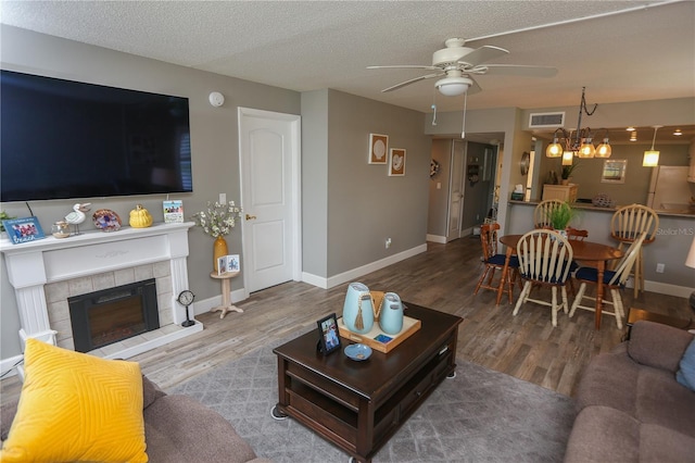 living room with a tiled fireplace, ceiling fan, a textured ceiling, and hardwood / wood-style flooring