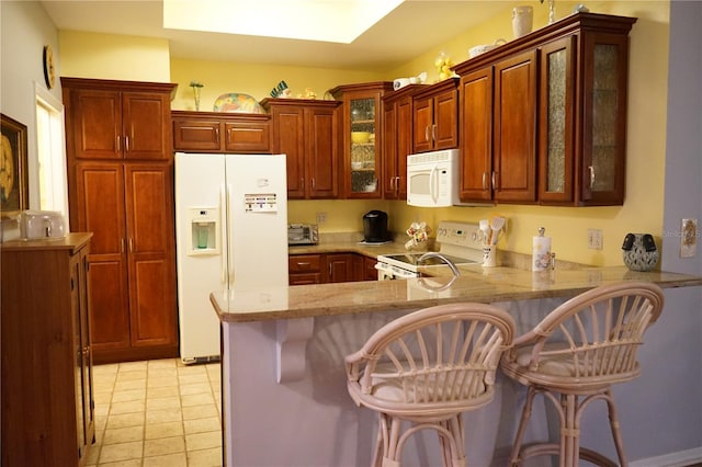 kitchen featuring light tile patterned floors, kitchen peninsula, a kitchen breakfast bar, and white appliances