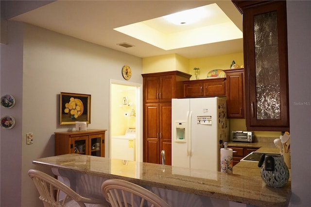 kitchen featuring a breakfast bar, white refrigerator with ice dispenser, washer / dryer, and kitchen peninsula