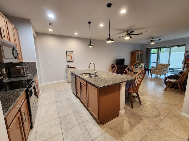 kitchen featuring appliances with stainless steel finishes, dark stone countertops, sink, hanging light fixtures, and a center island with sink