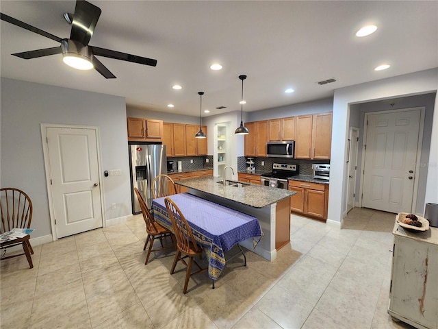 kitchen with an island with sink, ceiling fan, stainless steel appliances, pendant lighting, and sink