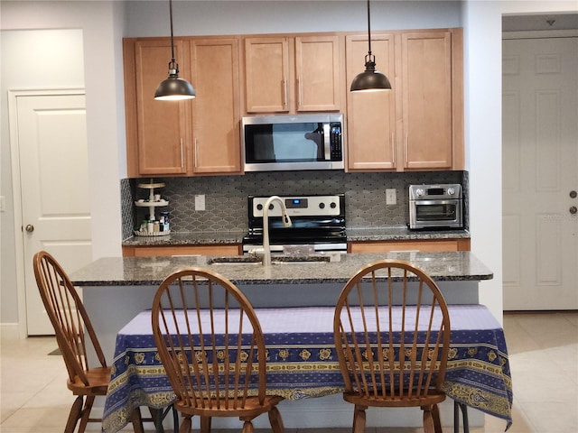 kitchen with decorative light fixtures, backsplash, dark stone countertops, stainless steel appliances, and light tile patterned floors