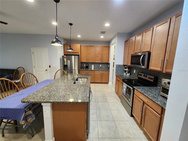 kitchen with decorative light fixtures, a center island with sink, a kitchen bar, decorative backsplash, and stainless steel appliances