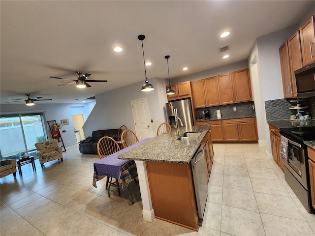 kitchen with decorative light fixtures, dark stone countertops, sink, a kitchen island with sink, and appliances with stainless steel finishes