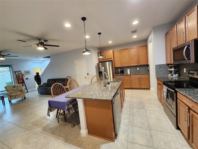 kitchen with decorative light fixtures, dark stone countertops, sink, appliances with stainless steel finishes, and an island with sink