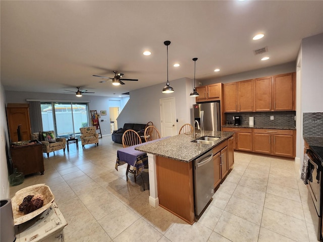 kitchen featuring a center island with sink, ceiling fan, appliances with stainless steel finishes, decorative backsplash, and hanging light fixtures