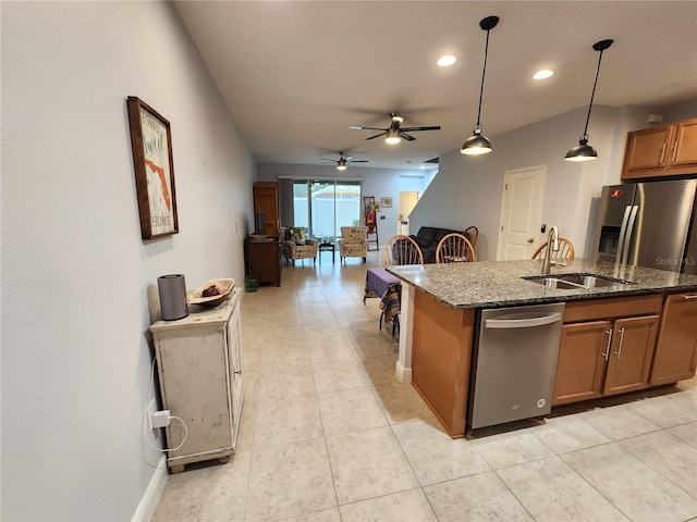 kitchen featuring decorative light fixtures, dark stone counters, an island with sink, sink, and ceiling fan