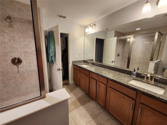 bathroom with a textured ceiling, tile patterned floors, a shower with shower door, and vanity