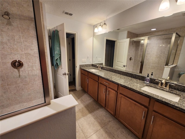 bathroom featuring a textured ceiling, tile patterned flooring, a shower with shower door, and vanity