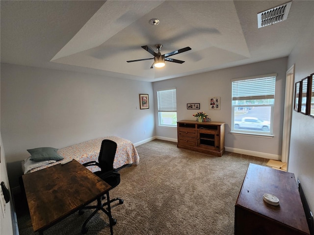 carpeted home office with ceiling fan, a textured ceiling, and a tray ceiling