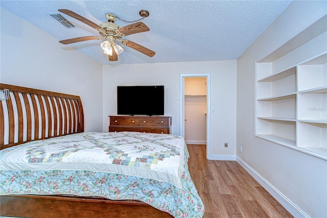 bedroom featuring ceiling fan, a spacious closet, light hardwood / wood-style flooring, a textured ceiling, and a closet