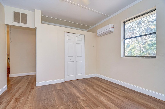 unfurnished bedroom featuring light hardwood / wood-style floors, an AC wall unit, and a closet