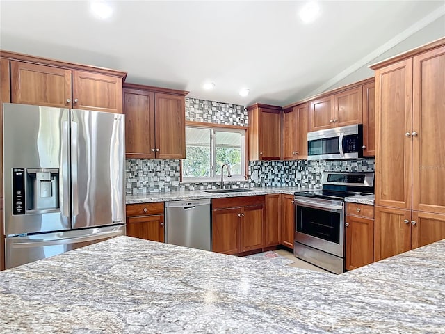 kitchen featuring appliances with stainless steel finishes, sink, backsplash, light stone counters, and lofted ceiling