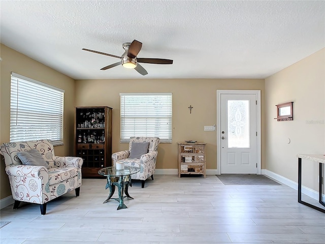 living area featuring ceiling fan, light hardwood / wood-style floors, and a textured ceiling