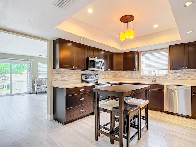 kitchen featuring stainless steel appliances, a raised ceiling, hanging light fixtures, and sink