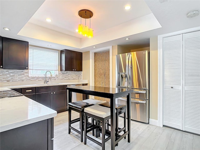 kitchen with dark brown cabinetry, sink, hanging light fixtures, stainless steel appliances, and a raised ceiling