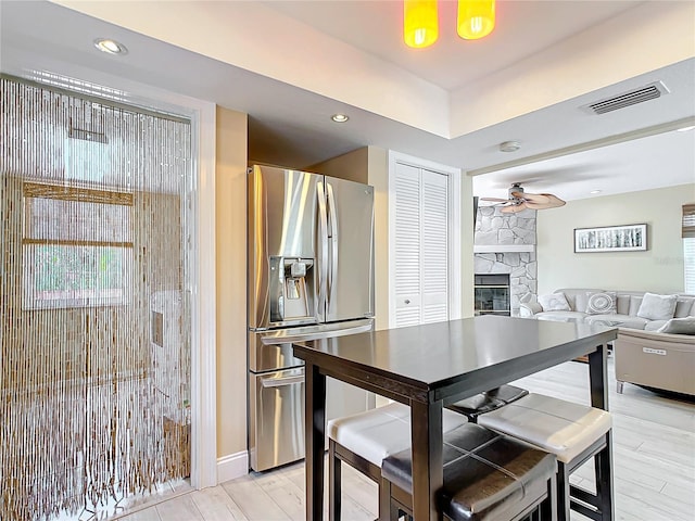 kitchen featuring stainless steel fridge with ice dispenser, a fireplace, ceiling fan, and light hardwood / wood-style flooring