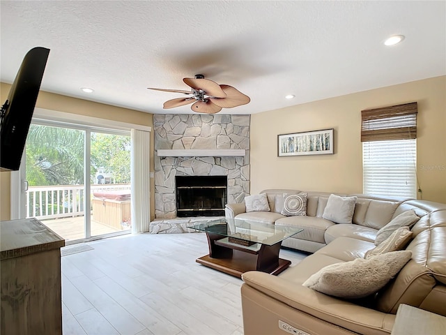 living room featuring a fireplace, a textured ceiling, light wood-type flooring, and ceiling fan