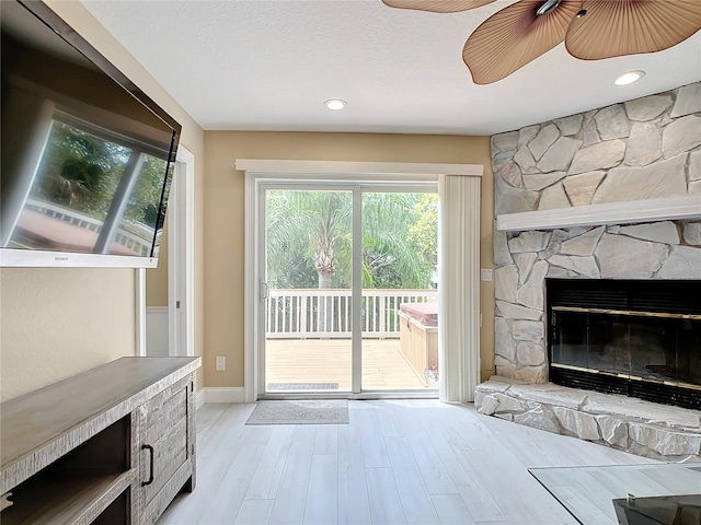 doorway with ceiling fan, light hardwood / wood-style floors, and a stone fireplace