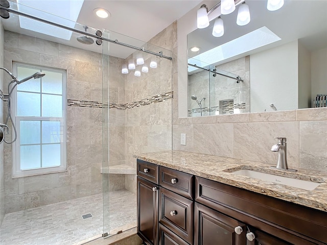 bathroom featuring vanity, backsplash, a skylight, and a shower with door