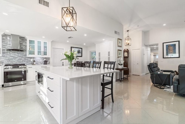 kitchen featuring white cabinetry, wall chimney exhaust hood, pendant lighting, and stainless steel range oven