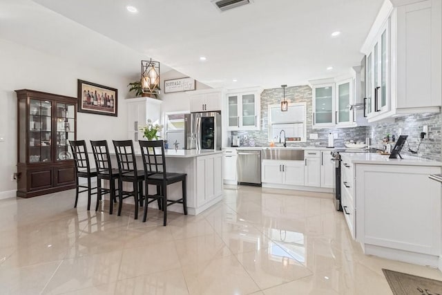 kitchen with a breakfast bar, hanging light fixtures, a kitchen island, white cabinetry, and stainless steel appliances