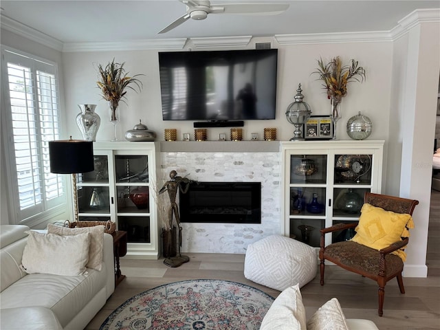 living room with a tiled fireplace, ornamental molding, wood-type flooring, and ceiling fan