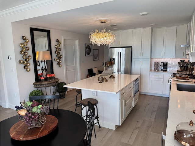 kitchen featuring a kitchen island, decorative light fixtures, built in microwave, white cabinets, and stainless steel fridge