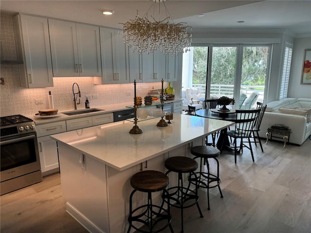 kitchen with a kitchen island, stainless steel gas stove, sink, crown molding, and light hardwood / wood-style flooring