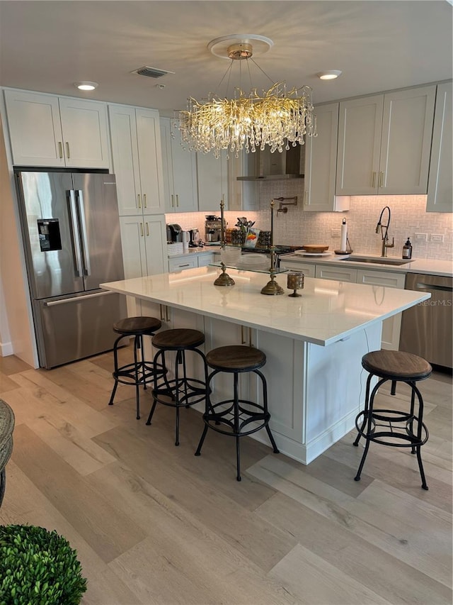 kitchen featuring white cabinetry, sink, a breakfast bar area, stainless steel appliances, and a center island with sink