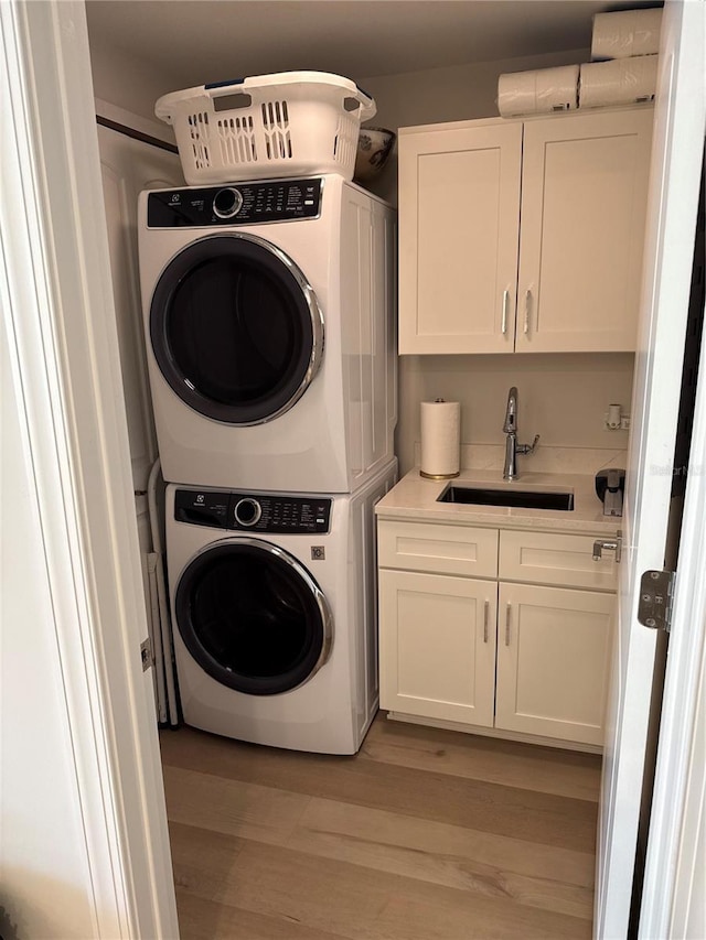 clothes washing area featuring cabinets, stacked washer and dryer, sink, and light wood-type flooring