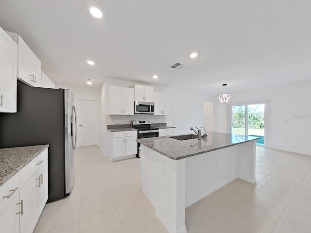 kitchen with stainless steel appliances, sink, white cabinetry, light stone counters, and an island with sink