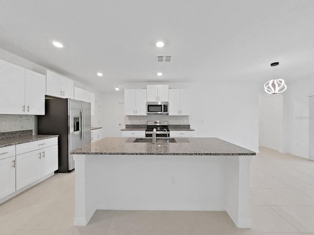 kitchen featuring appliances with stainless steel finishes, white cabinets, an island with sink, and decorative light fixtures